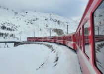a red train traveling down train tracks next to a snow covered mountain